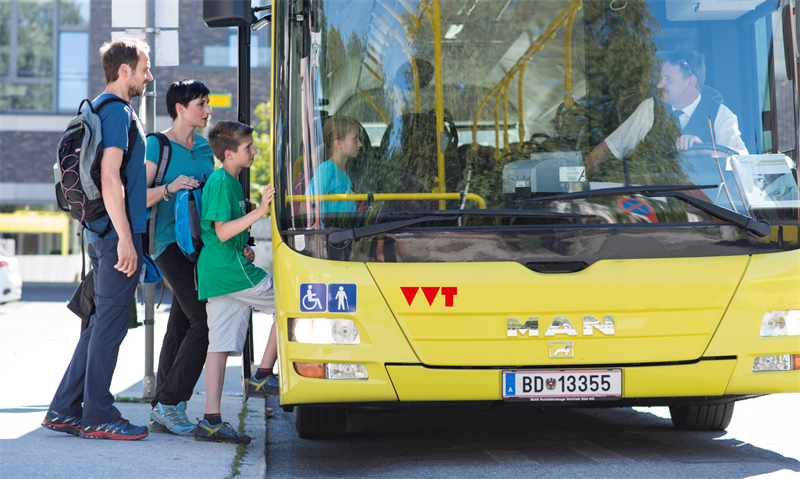 Eine Gruppe von Menschen steigt in einen gelben Bus des Verkehrsverbundes Tirol
